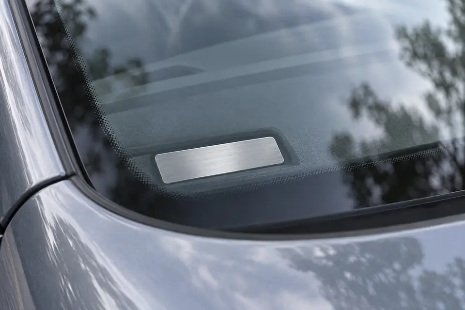 Lower corner of a windshield with the metal VIN plate on the dashboard, seen from outside the car